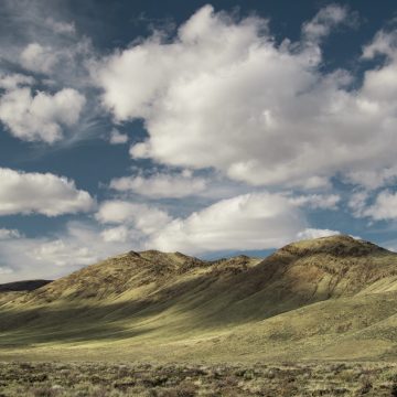 Fluffy clouds in a bright blue sky cast shadows on dry, golden-yellow hills