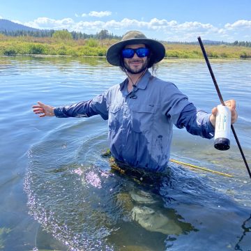 A researcher stands in waste deep water holding equipment in one hand.