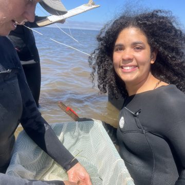 Research Fellow Maria Garcia kneels in water while holding a net.